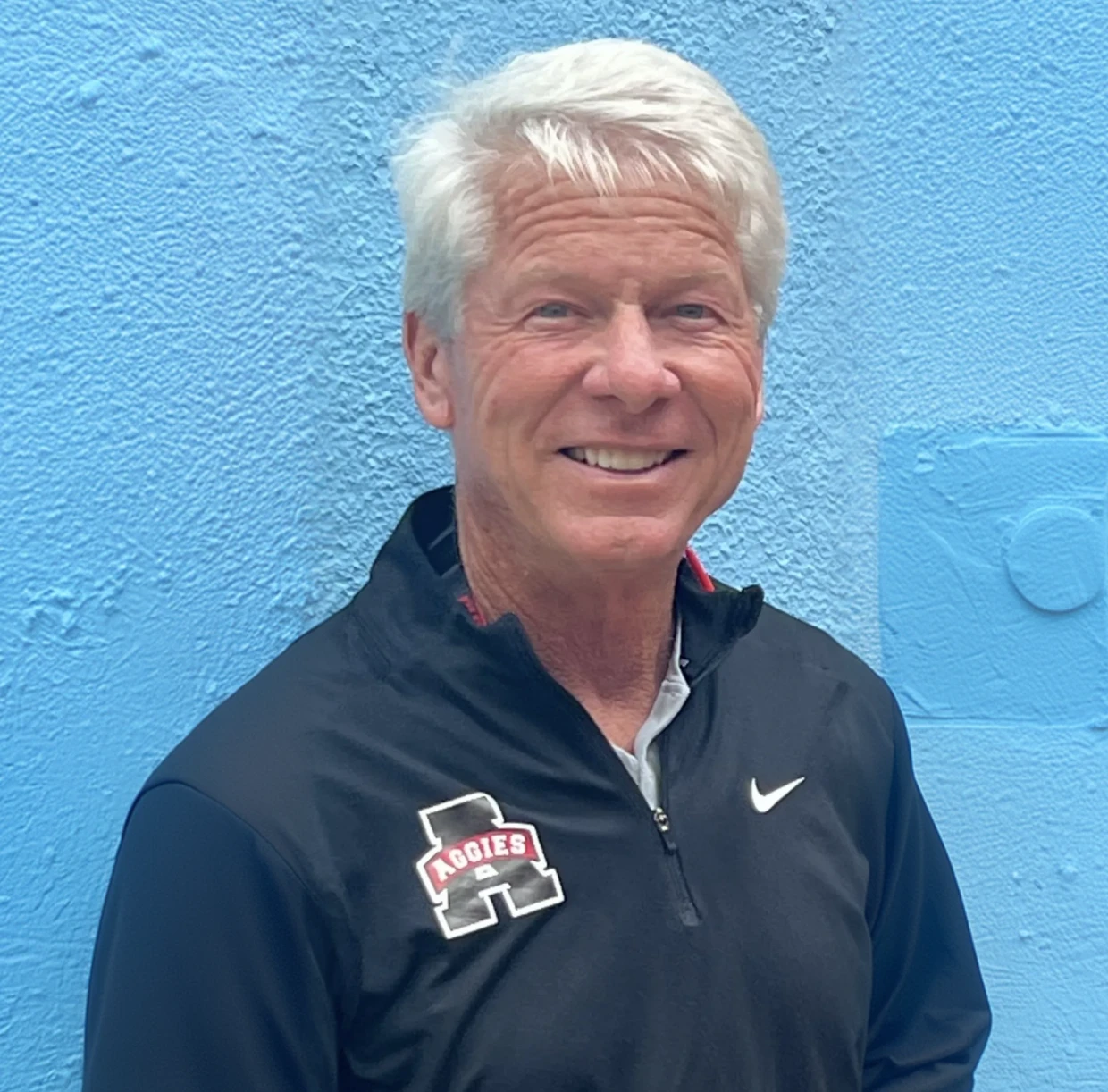 Smiling man in black jacket, blue background.