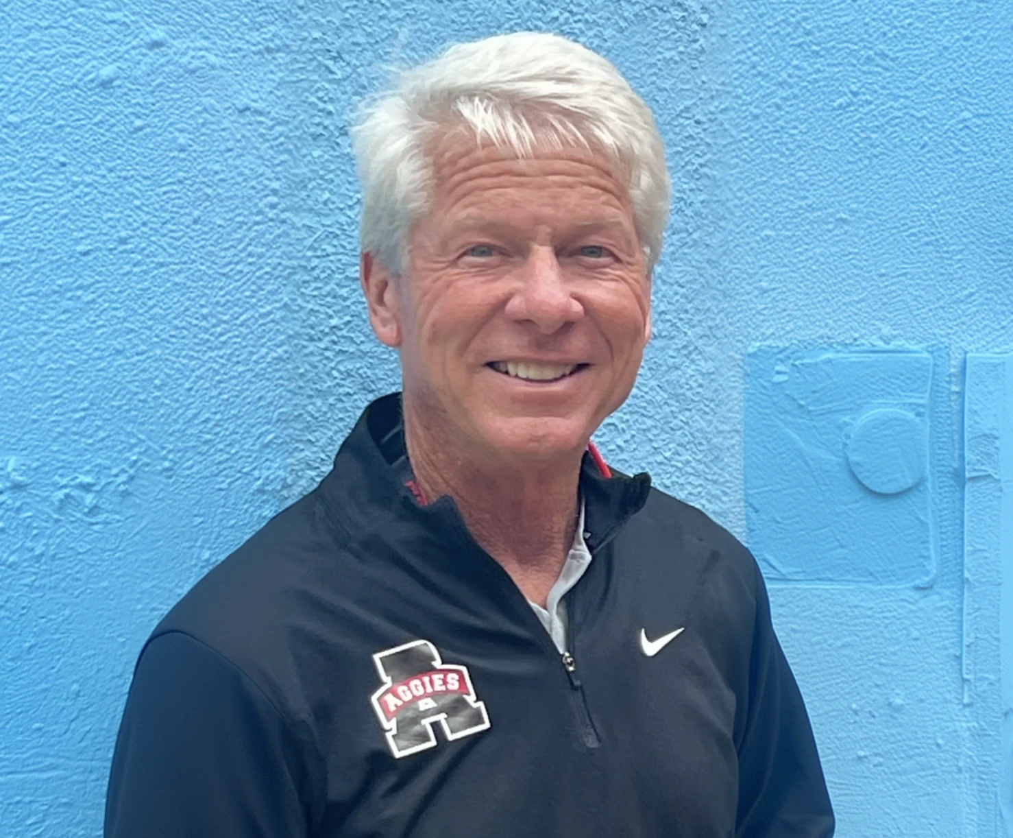 Smiling man in black jacket, blue background.